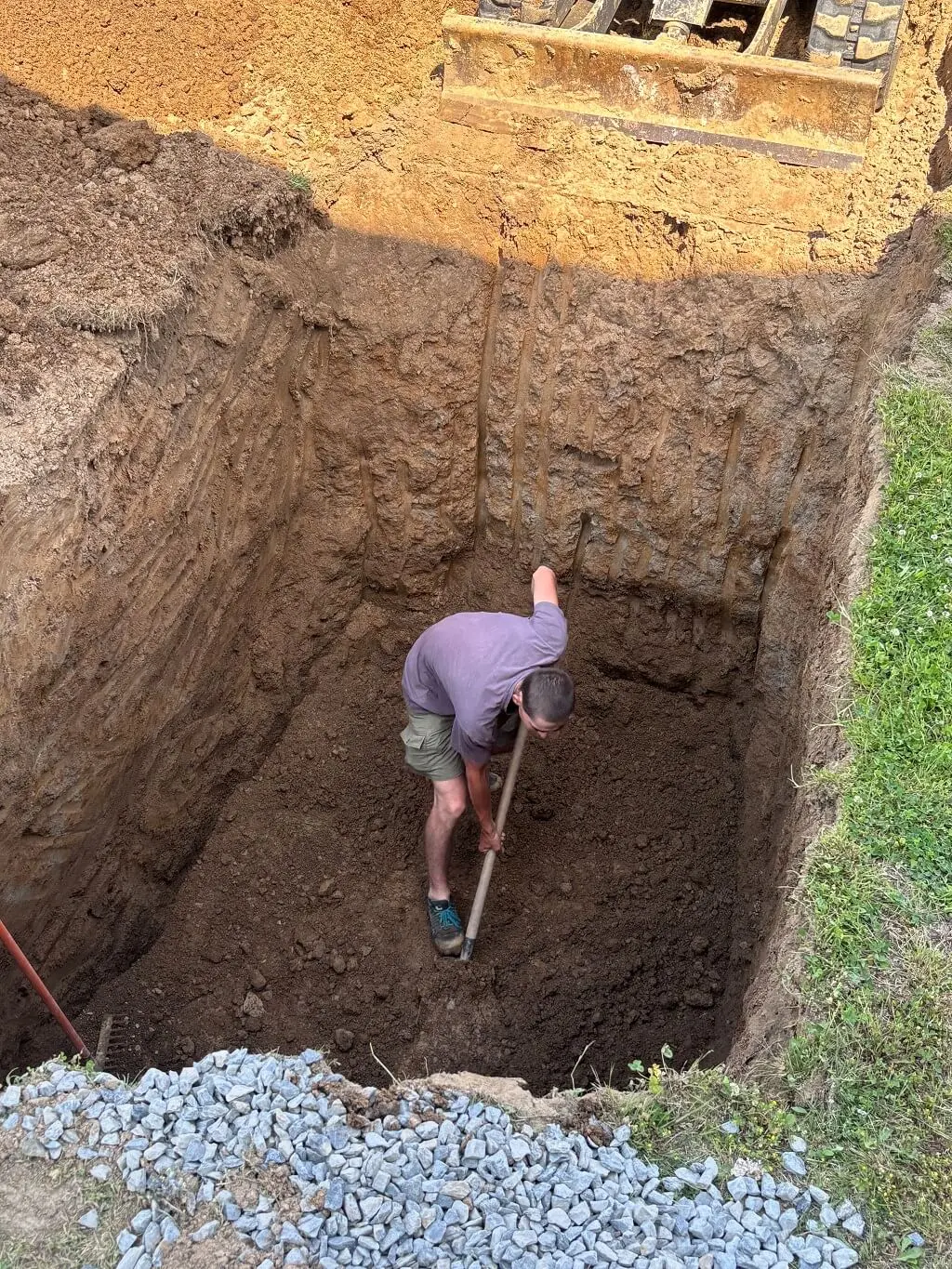 Pracovník ručně dočišťuje hluboký výkop pro nádrž